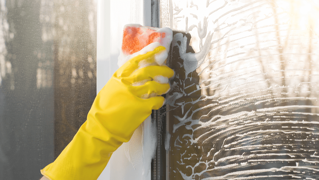 Person wearing glove washing a window with a sponge