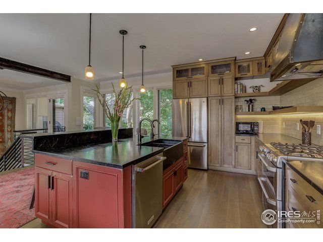 kitchen with cool tone wooden cabinets and a burgundy red island with three pendant lights and large windows