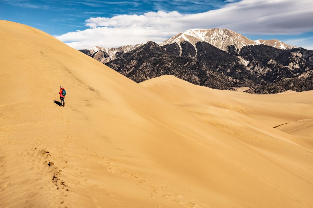 Person hiking on sand dune with mountains in background